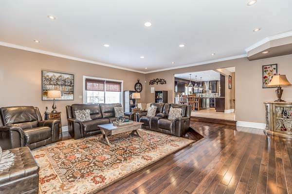 Living room with wooden walls, large windows, dark leather sectional sofa, and glass coffee table.